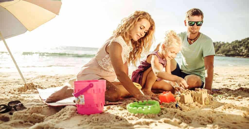 fillette construisant un château de sable avec ses parents