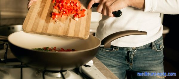 Une femme qui verse les tomates dans la poêle à wok