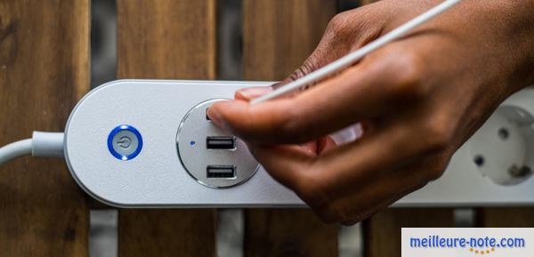 Une main qui branche un chargeur de smartphone sur une multiprise