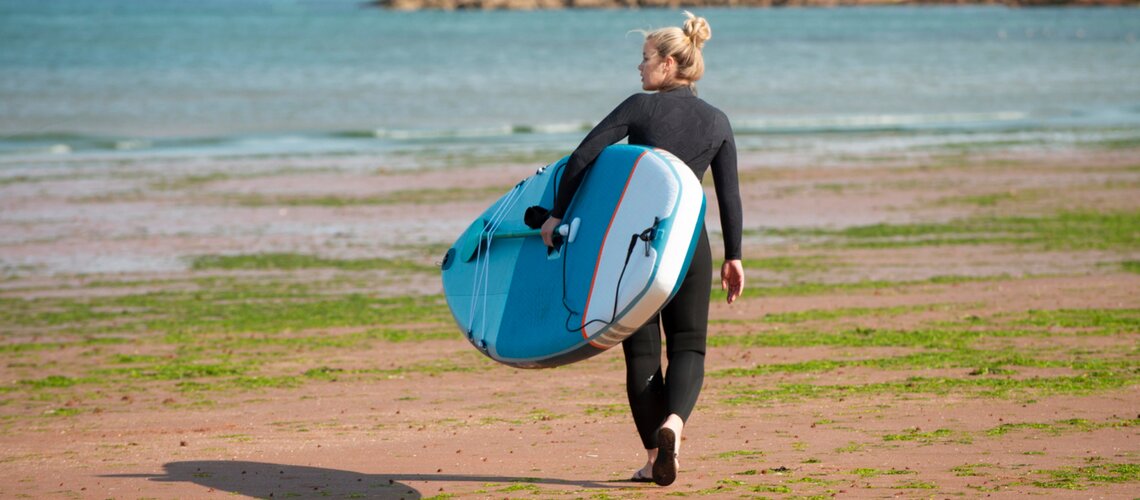 jeune femme qui transporte son paddle sur la plage