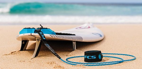 Une planche de surf et un leash de marque FCS