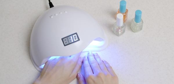 deux mains dans une sèche UV et des vernis semis permanent